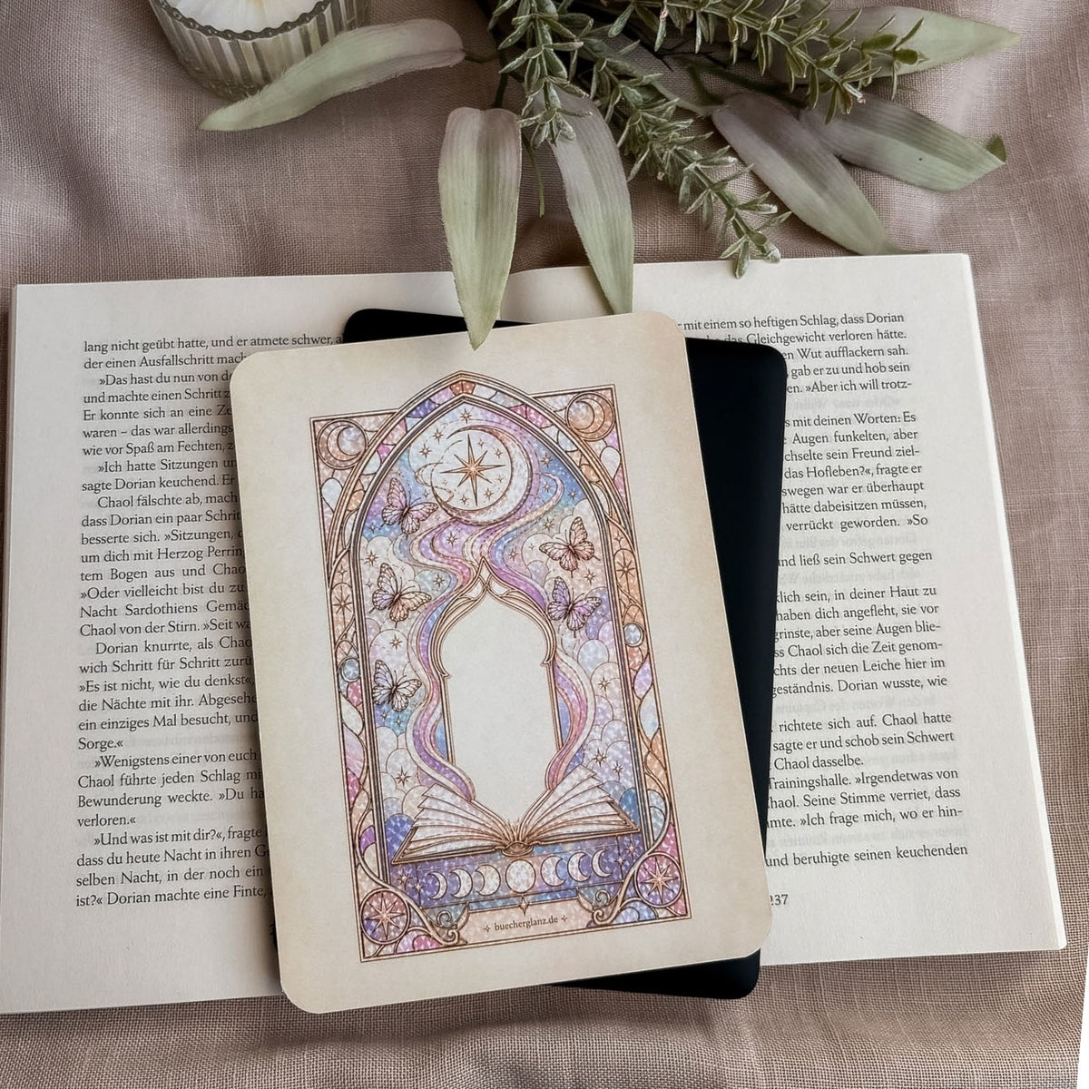 Divined Chapter E-Reader Insert im Buntglasdesign auf einem schwarzen E-Reader, darunter ein aufgeschlagenes Buch