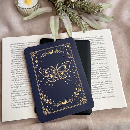 Enchanted Moth E-Reader Insert mit goldener Mondmotte auf einem schwarzen E-Reader, darunter ein aufgeschlagenes Buch