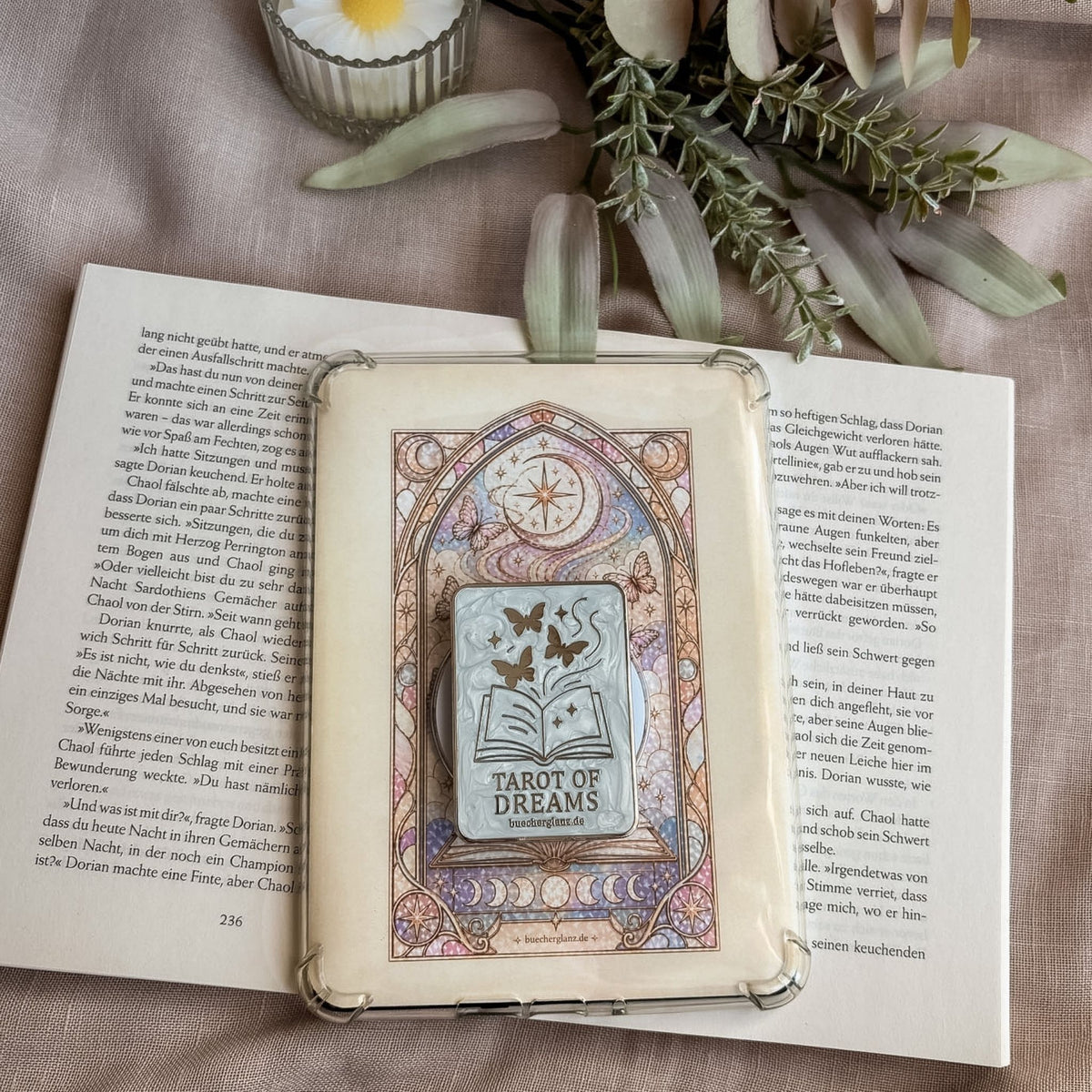 Divined Chapter Set: E-Reader Insert in transparenter Hülle mit dem passenden Grip auf einem aufgeschlagenen Buch