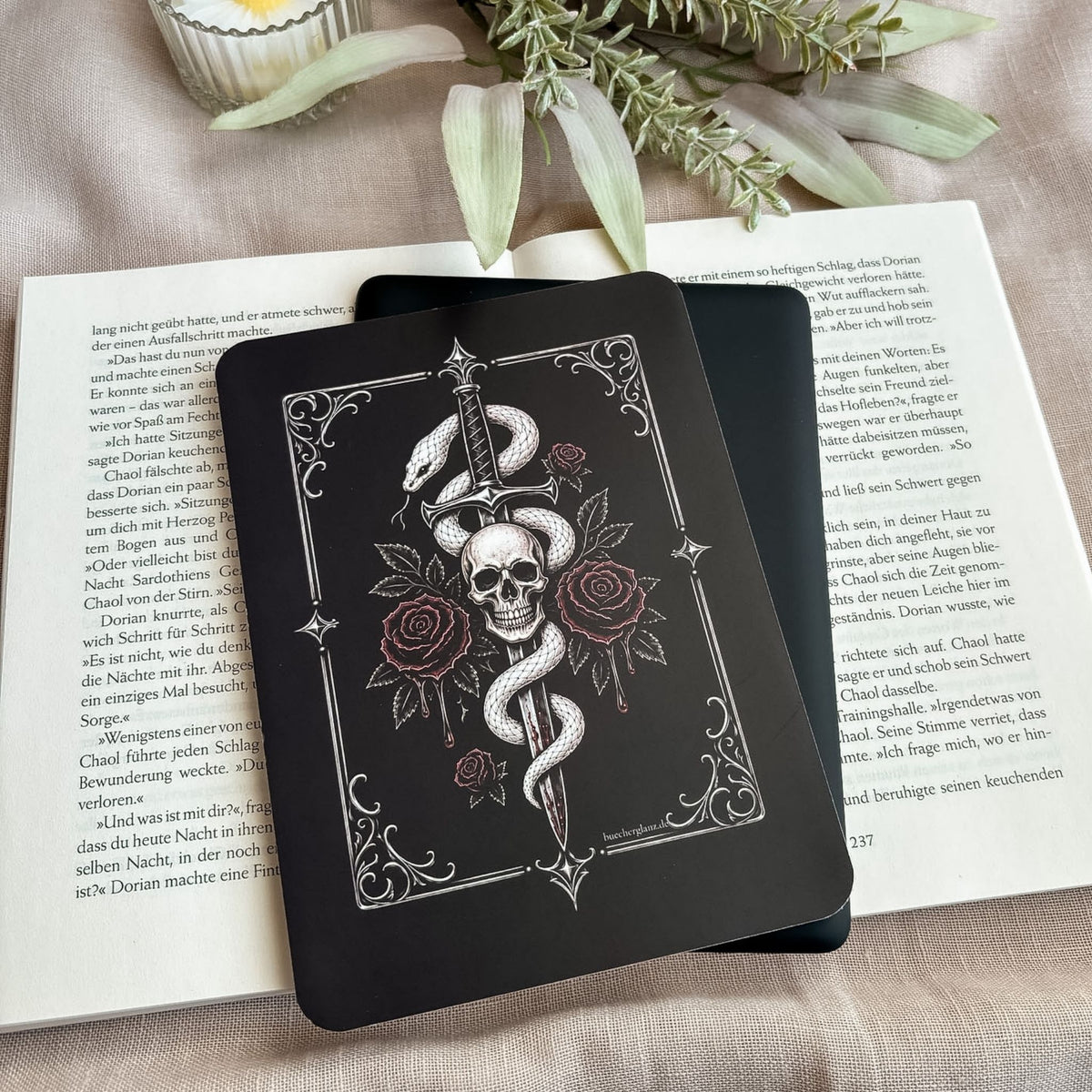 Tenderly Damned E-Reader Insert mit Schlange und Totenkopf auf einem schwarzen E-Reader, darunter ein aufgeschlagenes Buch