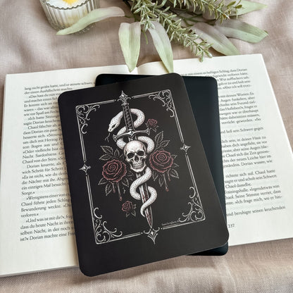 Tenderly Damned E-Reader Insert mit Schlange und Totenkopf auf einem schwarzen E-Reader, darunter ein aufgeschlagenes Buch