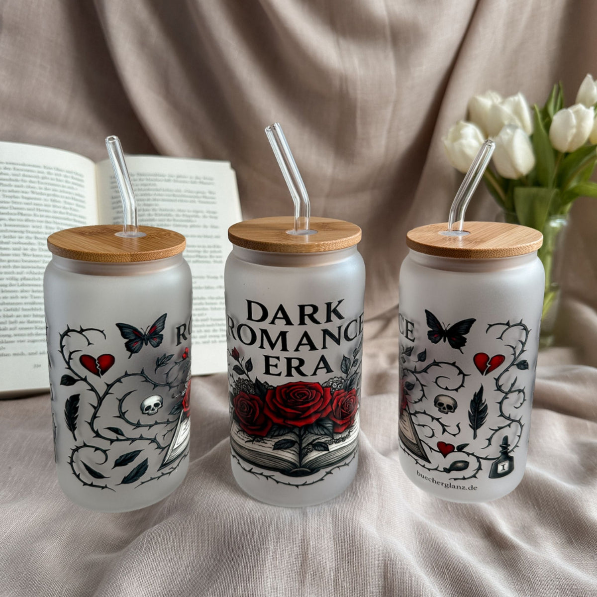 Frosted 16-oz-Glastumbler „Dark Romance Era“ mit roten Rosen und Gothic-Details neben offenem Buch und weißen Tulpen