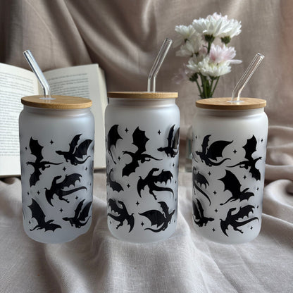 Frosted 16-oz-Glastumbler im Drachen-Design mit Bambusdeckel und Glasstrohhalm neben offenem Buch und weißen Blumen