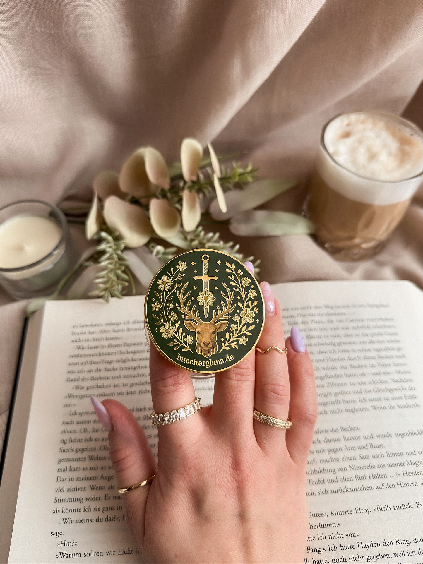 Heir of the Forest Kindle Grip Silber – in Hand gehalten auf aufgeschlagenem Buch, Romantasy Design mit Hirsch, Schwert und Blumen, Silberrand, buecherglanz