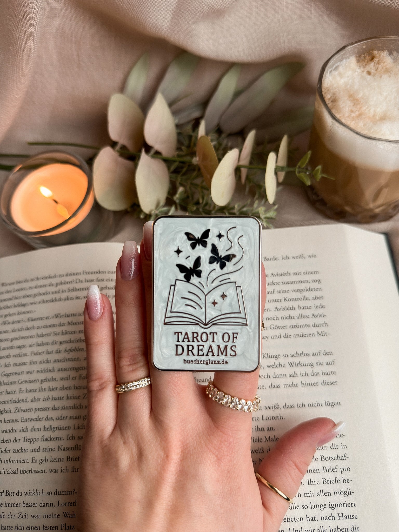 Tarot of Dreams Kindle Grip in Hand auf aufgeschlagenem Buch mit Kerze und Latte