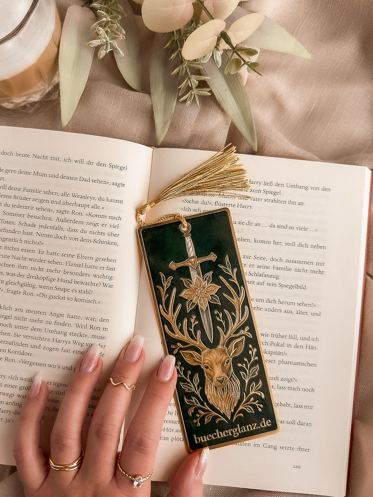 The Verdant Vow metal bookmark with gold tassel in an open book, held in hand