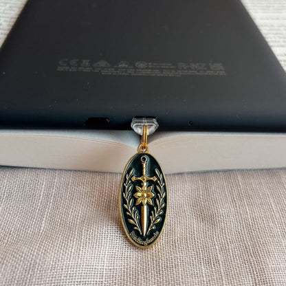 Blade & Bloom USB-C Charm Plug in Gold mit Schwert-, Blüten- und floralen Details am schwarzen E-Reader auf offenem Buch