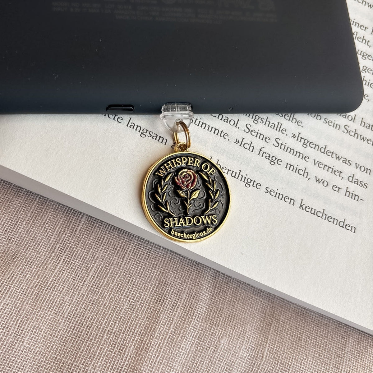 Whisper of Shadows USB-C Charm Plug mit roter Rose und goldenen Details am E-Reader auf offenem Buch