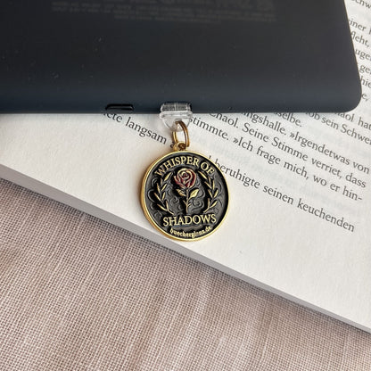 Whisper of Shadows USB-C Charm Plug mit roter Rose und goldenen Details am E-Reader auf offenem Buch