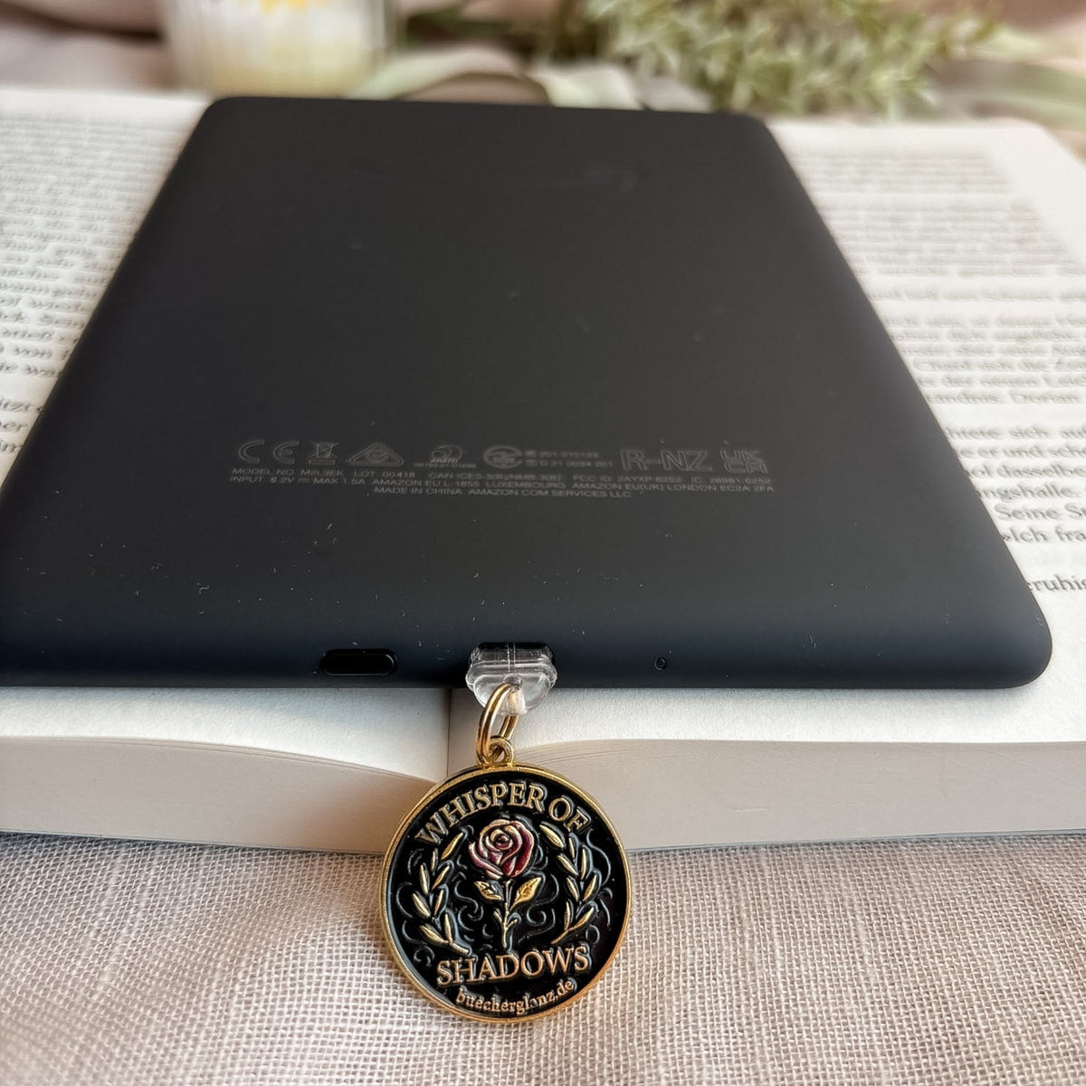 Whisper of Shadows USB-C Charm Plug in Gold am schwarzen E-Reader mit Rosenmotiv auf offenem Buch