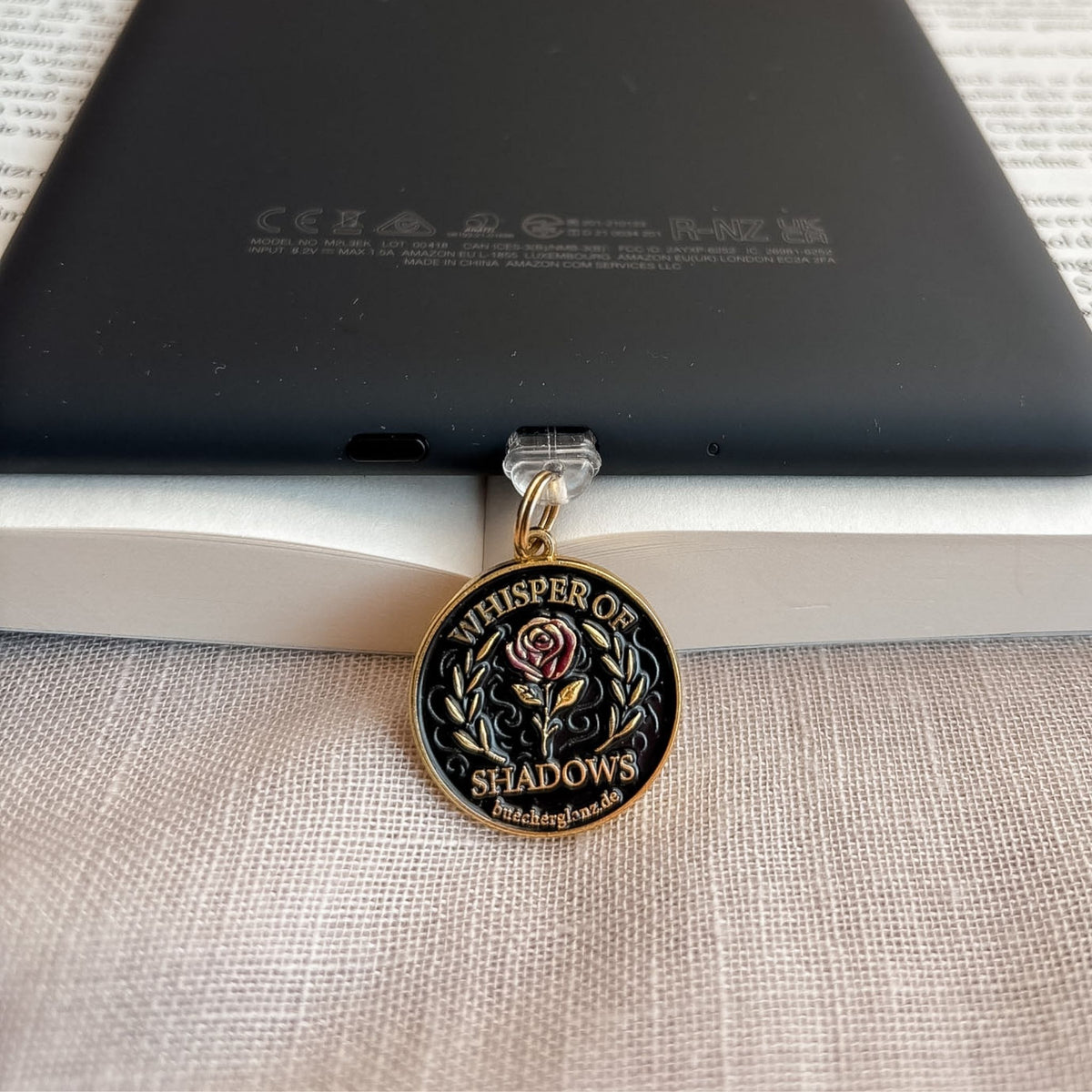 Whisper of Shadows USB-C Charm Plug in Gold am schwarzen E-Reader mit Rosenmotiv auf offenem Buch